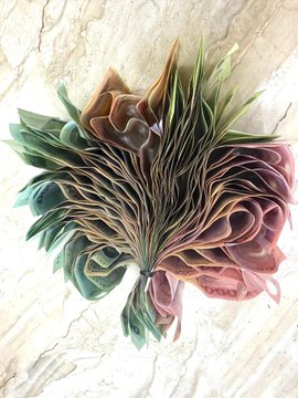 A decorative arrangement of handmade fabric flowers in shades of green, brown, and pink, resting on a marbled surface.