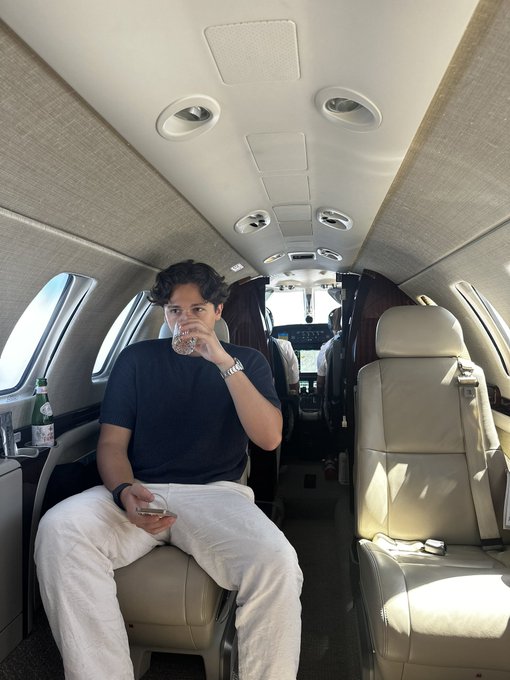 A young man relaxes inside a private jet, sipping from a glass while holding his phone, embodying the luxury lifestyle associated with the crypto gains mentioned in the post about $BTC, $LIT, $SOL, and $ETH. The image reinforces the "we're going much higher" message by visually showcasing the rewards of successful trading.