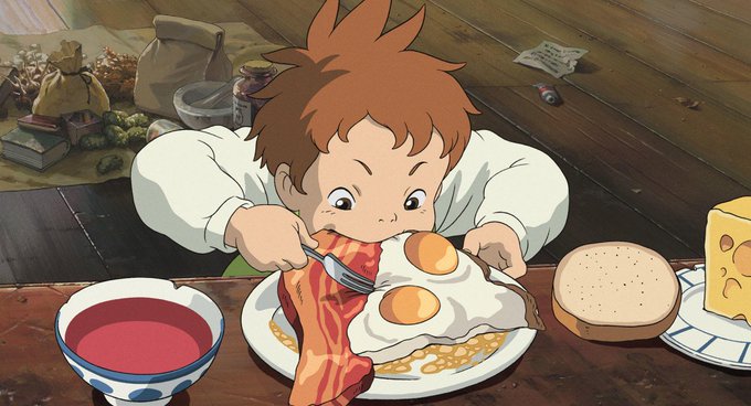 An animated scene of a young boy with reddish-brown hair eagerly eating a large breakfast of bacon, eggs, beans, and toast at a wooden table, with cheese and a bowl of red sauce nearby.