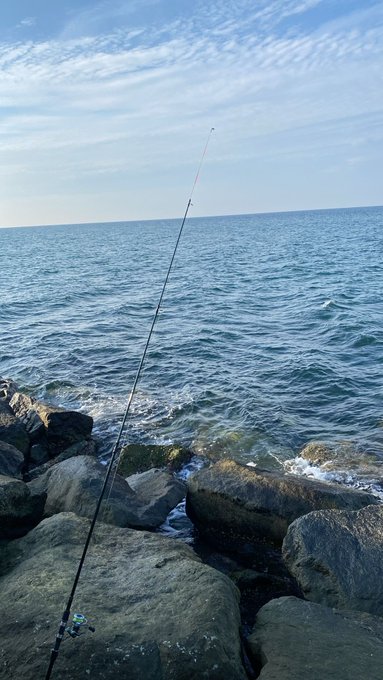 A fishing rod extends from the rocks into the sea under a partly cloudy sky, suggesting a coastal fishing setup.