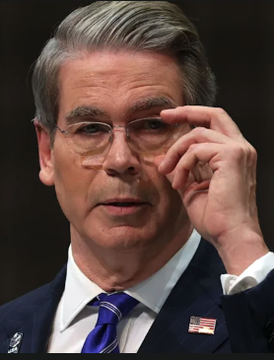 A man in a dark suit with an American flag pin and blue tie adjusts his glasses, appearing to speak at what looks like a formal event or hearing. The image likely depicts U.S. Treasury Secretary Scott Bessent, who is associated with the announcement of a $6 billion bond buyback plan aimed at improving bond market liquidity and potentially easing pressure on yields to benefit stocks and crypto markets.
