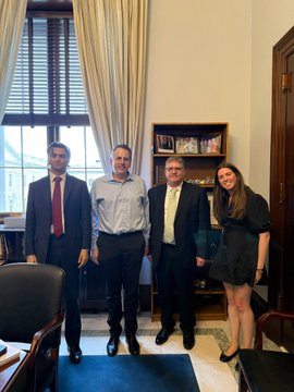 Group photo of four people (three men and one woman) posing together in what appears to be an official indoor setting with curtains and framed photos in the background.