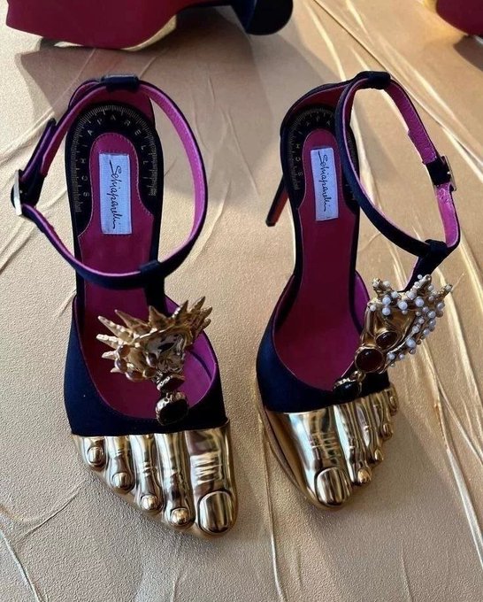A pair of Schiaparelli high-heeled sandals featuring dark purple straps, gold foot sculptures with toe details, and jeweled embellishments on the ankle straps.