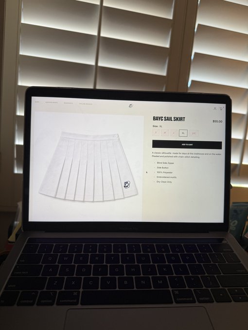 A MacBook Pro on a desk displaying an online product page for a white pleated "Bayc Sail Skirt" priced at $55.00.
