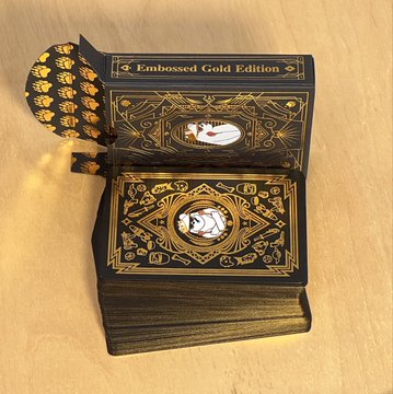 A thick stack of black playing cards with gold foil embossing, labeled 'Embossed Gold Edition' on the box, featuring ornate designs and a central circular emblem on the top card.
