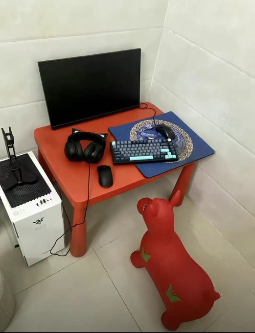 A small red children's table holds a monitor, headphones, mouse, and keyboard on a Van Gogh-themed mat, with a red inflatable punching toy on the floor beside a PC tower.