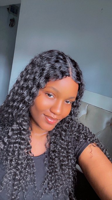 A young woman with long, dark curly hair smiles softly at the camera in a selfie-style portrait.