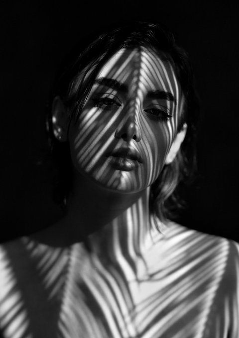 A black-and-white portrait of a woman with striped shadows cast across her face and neck.