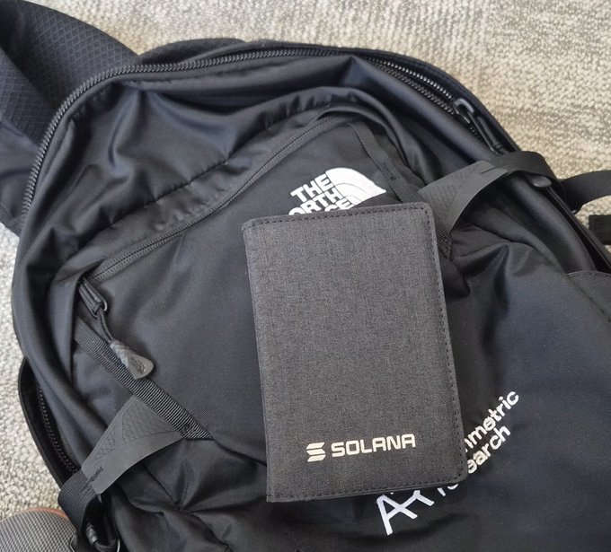 A black Solana cardholder wallet resting on top of a black North Face backpack on a carpeted floor.