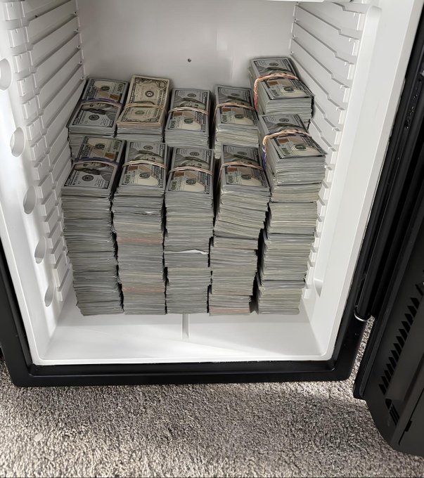 The interior of a white mini-fridge or cooler is completely packed with numerous bundles of US dollar bills stacked neatly from the bottom up.