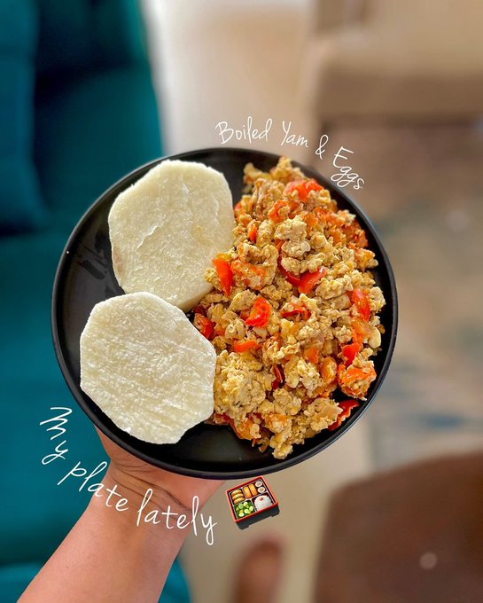 A hand holds a black bowl containing boiled yam slices and scrambled eggs with tomatoes, labeled "Boiled Yam & Eggs" with the caption "This plate lately," playfully responding to the "Have you eaten?" prompt.