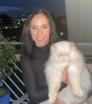 A woman with dark hair smiles while holding a fluffy cream-and-tan Persian cat with a distinctive flat face, likely a "rancat" NFT, set against a twilight balcony backdrop. The image aligns with her post about sharing feline art inspiration, though no specific text or tickers are clearly visible in the picture itself.