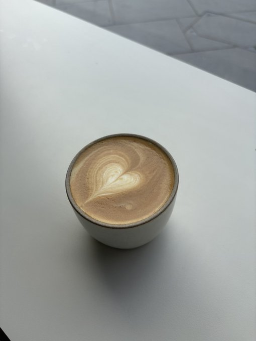 A cup of coffee with heart-shaped latte art sits on a white table.