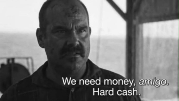 A black and white movie still features a man with a mustache looking sternly at the camera, with subtitles reading 'We need money, amigo. Hard cash.'