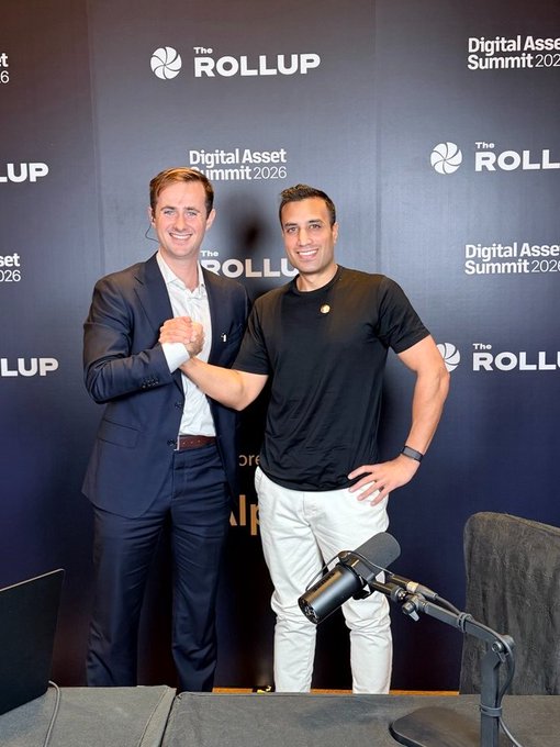 Two men in business attire shake hands in front of a backdrop reading 'The Rollup Digital Asset Summit 2026'.