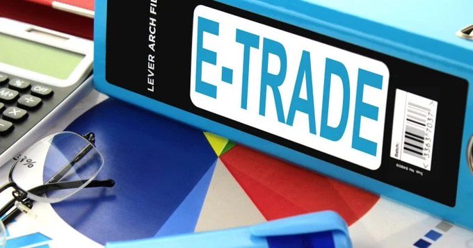 An E-Trade lever arch file rests on a colorful pie chart beside a calculator and eyeglasses, suggesting financial planning or trading documentation.