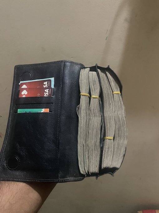 An open black leather wallet stuffed with thick bundles of cash held together by rubber bands, with Visa and other cards visible in the card slots.