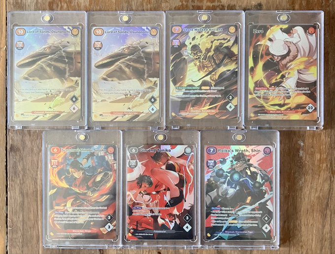 A collection of seven Azuki TCG trading cards displayed in protective sleeves on a wooden surface, including "Lord of Sands, Osunaga" (x2), "Stone Mason's Ancient," "Shao," "Steel-Heart Shinobu," "Shinobi, Tanika," and "Raiko's Wrath, Shin." The image showcases the poster's AA SR pulls from Azuki TCG booster boxes, complementing their question about whether to open the remaining 3 sealed boxes.
