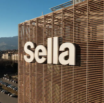 The image shows a large building with a sign that reads "SELLA" written in white letters, which appears to be an advertisement for Bitcoin or cryptocurrency. The building also has a lot of windows, giving it a modern and sleek appearance. The photo is taken from an aerial perspective, providing a comprehensive view of the structure and its surroundings.