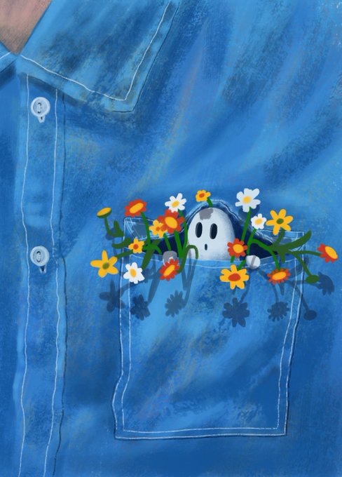 A close-up of a blue denim shirt featuring a painted design of a small ghost-like figure surrounded by colorful flowers in the breast pocket.