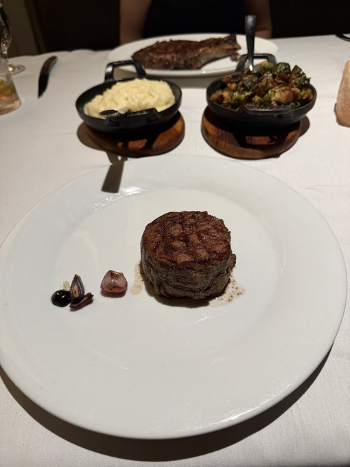 A plate of food including a filet mignon with a side of mashed potatoes and brussels sprouts in small skillets at a restaurant table.