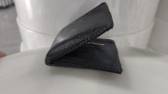 The image features a black leather wallet placed on top of a white surface, possibly a table or countertop. The wallet appears to be slightly open, revealing its contents inside. There are no visible texts or other objects in the scene.