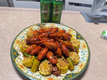 A plate of cooked crawfish served over corn on the cob and vegetables, with two green cans of beer in the background on a table.