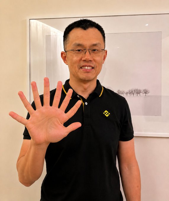 A man wearing glasses and a black polo shirt with a Binance logo holds up his open palm toward the camera, with an $80 million illegal funds claim referencing "criminal chinaman $CZ" displayed alongside.