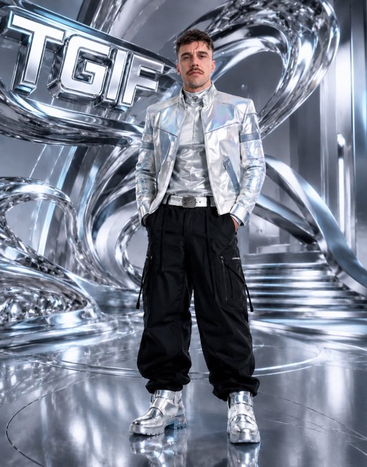 Man with a mustache standing in a futuristic silver metallic environment wearing a shiny silver jacket and chunky silver shoes, with "TGF" text visible in the background.