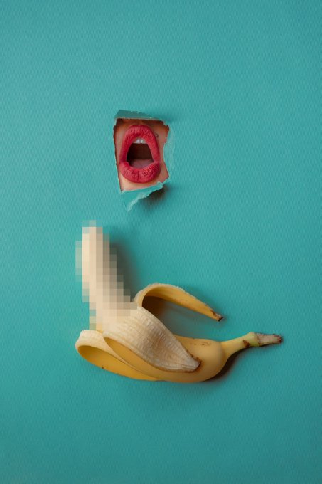 A surreal image of a peeled banana on a teal background, with a small torn-paper style cutout above it showing red lips, while part of the banana is pixelated.