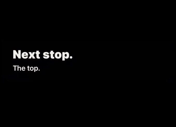 A minimalist black screen with the text 'Next stop.' in large white letters and 'The top.' in smaller white letters below it.
