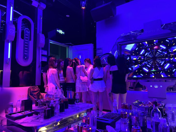 A group of women gathered at a bar or lounge illuminated by purple and blue neon lighting.