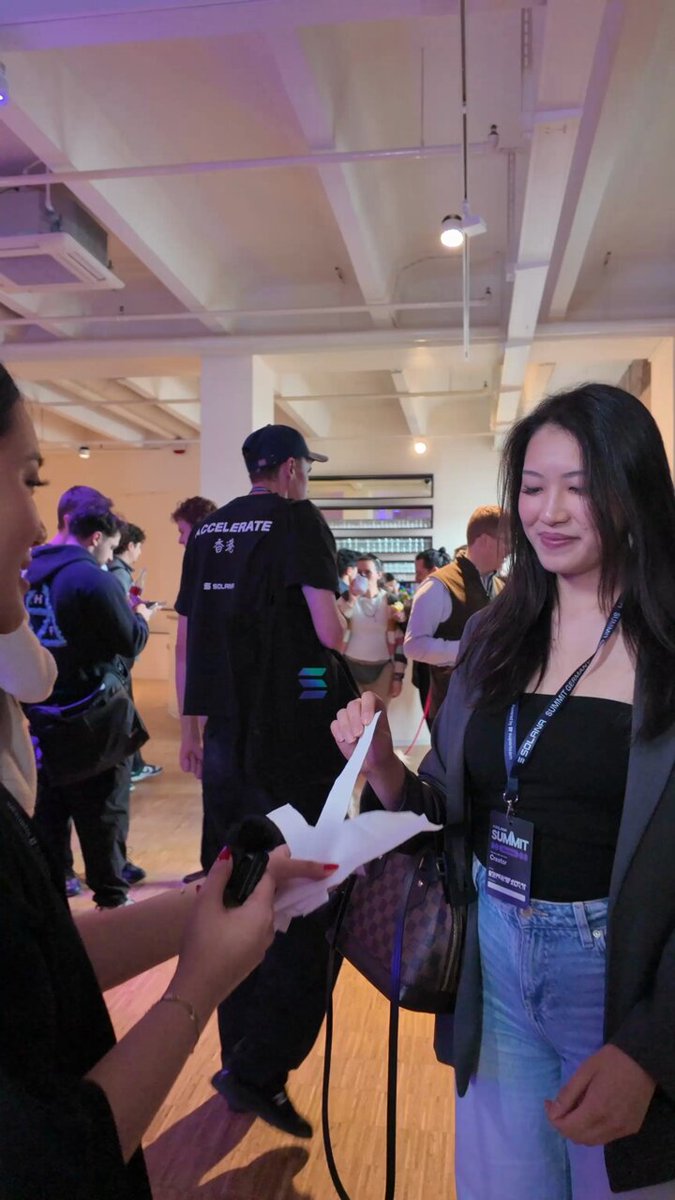 The image shows a woman holding up her hand for another person to shake, possibly at an event or gathering. There are several other people present in the scene, indicating that this could be a social event or a public place where people gather. The photo is captioned with "Solana Summit Germany edition" and "focus on what is in the image".
