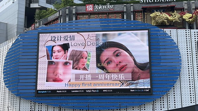 An outdoor LED screen in an urban area displays an advertisement for 'Love Design' starring Kao Aokbab, celebrating its first anniversary with the text '开播一周年快乐' and 'Happy first anniversary'.