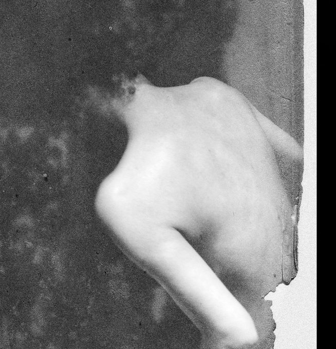 A grainy black and white photograph of a nude figure from behind, appearing to be an old artistic photograph.