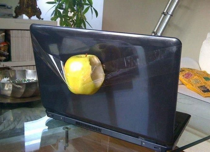 A flat-screen monitor displaying an image of a partially eaten green apple, placed on a glass table in a living room setting.