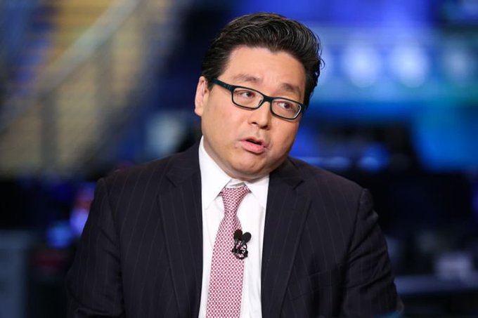 A man in a dark pinstripe suit, white shirt, and pink patterned tie speaks during what appears to be a Bloomberg TV interview, wearing glasses and a lapel microphone.