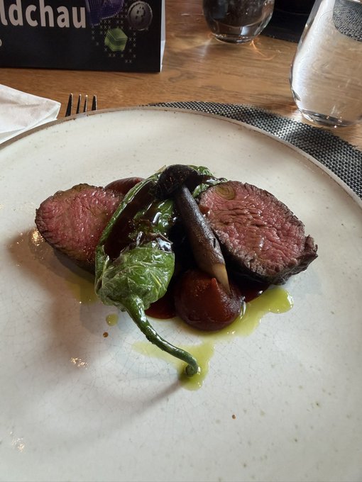 A plated meal featuring medium-rare beef slices, mushrooms, and spinach drizzled with sauce, served on a white dish at a restaurant table.
