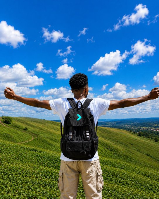 A hiker with arms outstretched stands atop a green hill under a bright blue sky, wearing a black backpack featuring a teal "greater than" symbol (>). The image visually echoes the post's message of forward momentum and freedom, suggesting that with the right tool, your finances can move you ahead—beyond limits—on your own terms.