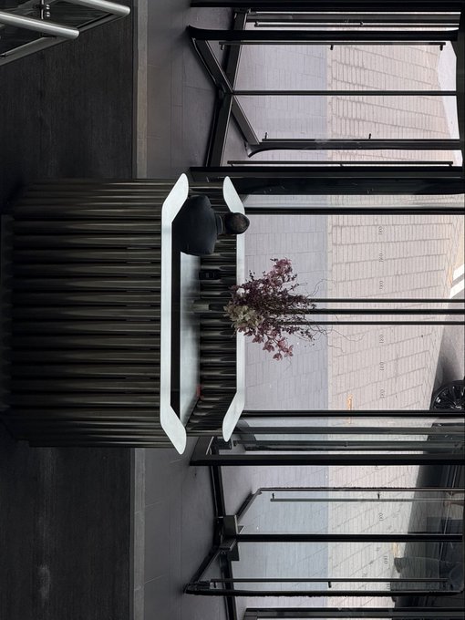 An overhead (rotated 90°) view of a dark wooden slatted counter or table with a white object, a small bouquet of flowers, and black-framed glass panels.