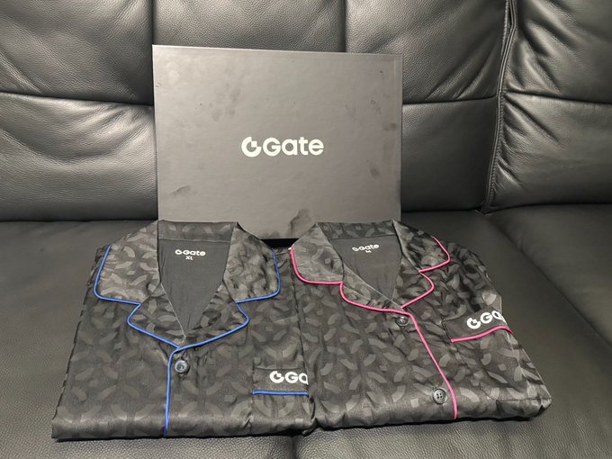 Two folded pajamas with a camouflage/leaf pattern, one with blue piping and one with pink piping, displayed with a 'Gate' branded gray envelope on a black leather couch.