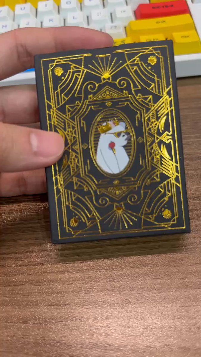The image features a hand holding up a small black book, which appears to be a card from the @SuperRare_Bears poker game. The card has a gold frame around it and depicts a woman with a red rose. The text on the card reads "Here are some Pro Poker Playing cards from @SuperRare_Bears you can +add+ to your amazing collection! They will be available in the @xPortalApp at dapp.woodenpunks.com in about a month".