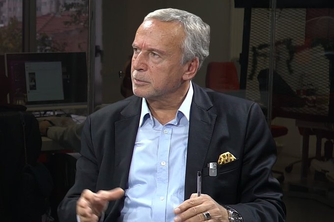 Ramazan Başak, former MASAK Deputy President, speaks during an interview while holding a pen, with a pocket square visible in his dark blazer over a light blue shirt. The image accompanies a statement about his past detentions related to his complaint against Tera, which was liquidated by the SPK.