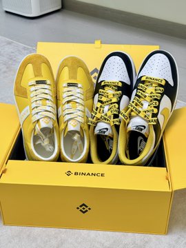 An open yellow Binance shoebox contains two pairs of sneakers (yellow and white) branded with Binance logos and styling.