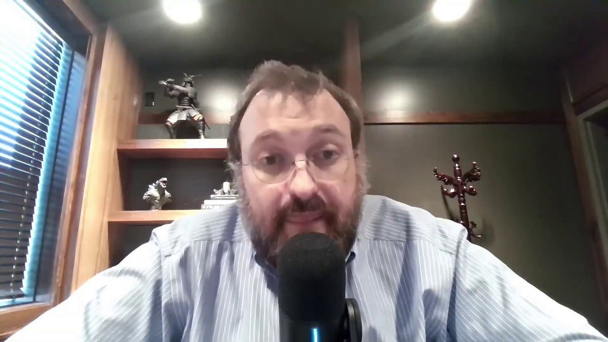 The image shows a man wearing glasses sitting at a desk with a microphone, likely preparing for a podcast recording or live stream. He has a beard and appears to be looking directly into the camera. The caption "RIP Cardano" is visible in the image, which could potentially be related to the post he's about to create on his podcast.