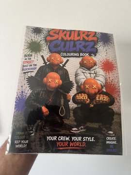 A hand holds a 'Skullz Culrz COLOURING BOOK by KAJ' cover featuring stylized skull characters with the tagline 'YOUR CREW, YOUR STYLE, YOUR WORLD.'