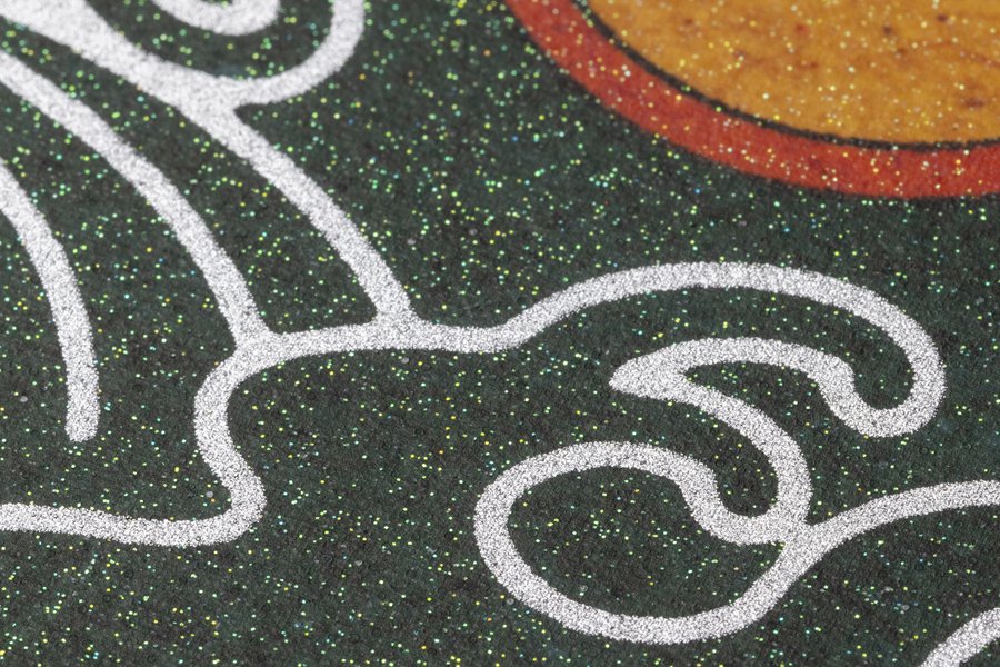 A close-up photograph shows a section of pavement or fabric with white swirling line art and a speckled black background next to a partial orange and red circular design.