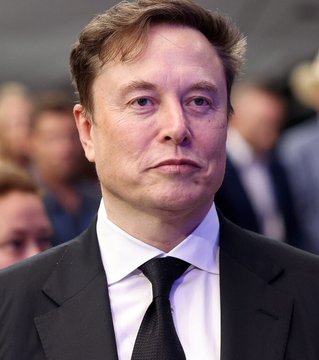 A close-up photo of Elon Musk in a dark suit and tie with a serious expression, accompanying news that he expressed "highly confident" SpaceX ($SPCX) will launch Nvidia ($NVDA) AI computers in space next year. The image directly illustrates the subject of the announcement, showing the SpaceX CEO whose company is making the ambitious AI-in-space claim.