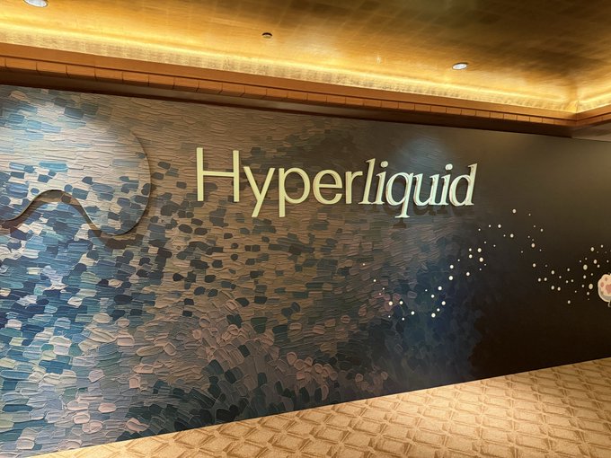 An indoor space featuring a decorative dark blue textured wall with the word 'Hyperliquid' displayed in large, illuminated gold lettering.