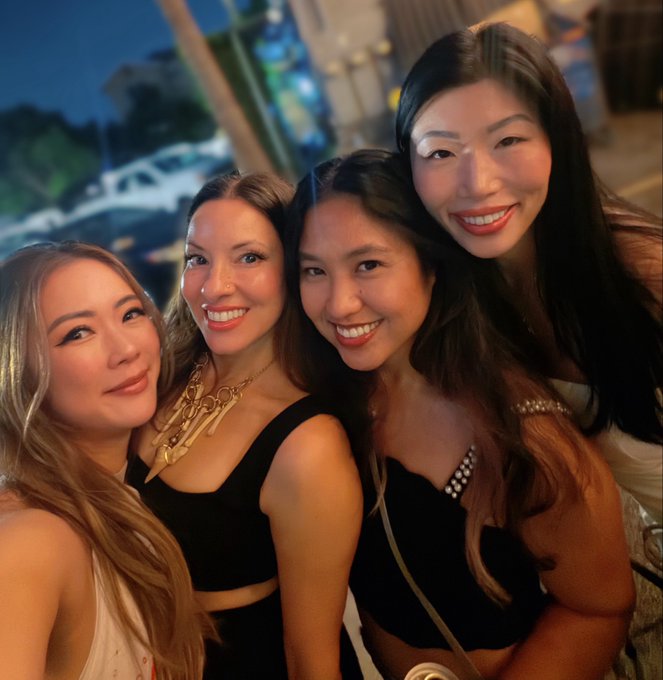 Four women pose together for a nighttime selfie, smiling at the camera in what appears to be an outdoor social setting.